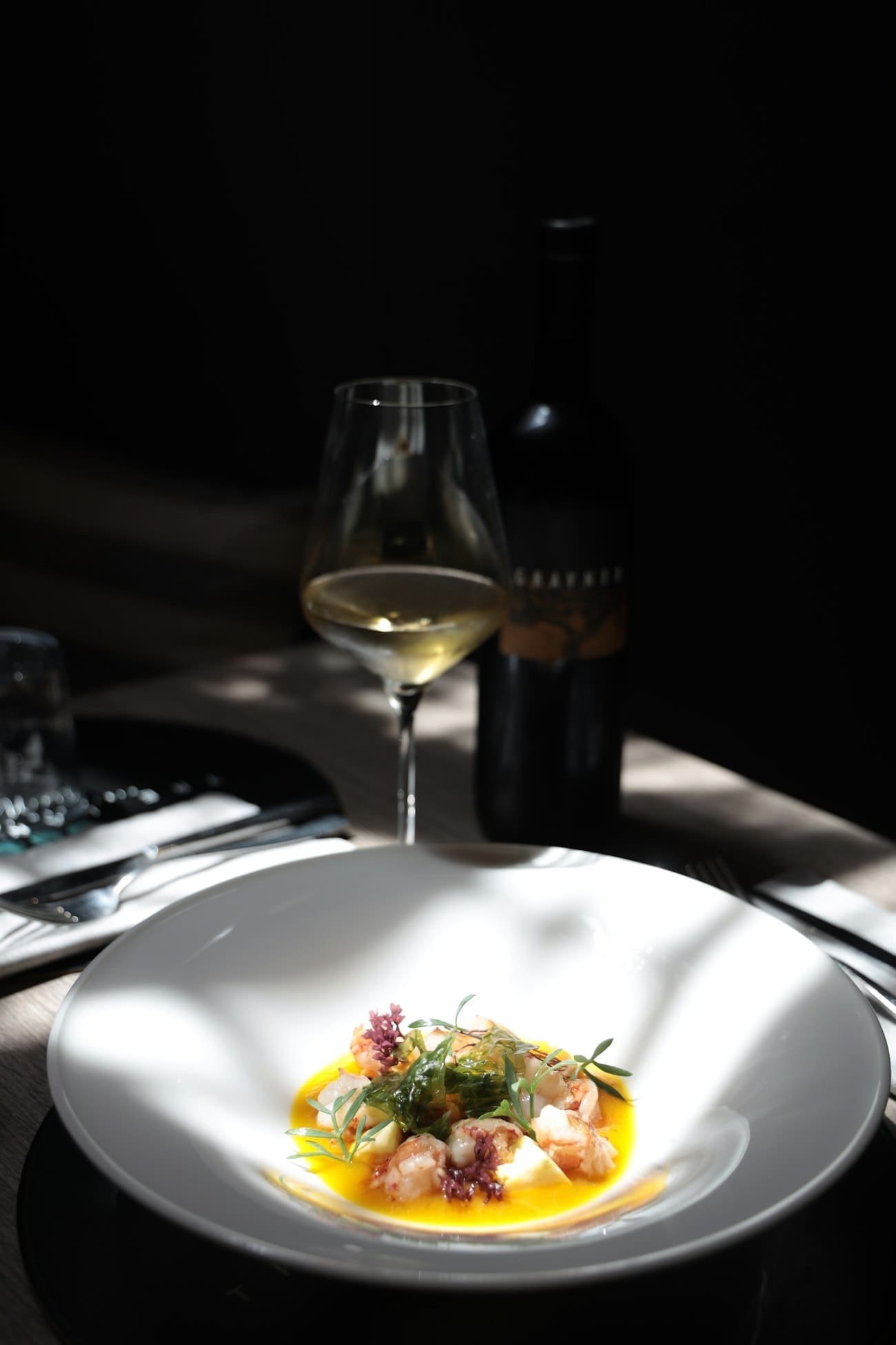 Plato de autor con vino blanco en mesa oscura